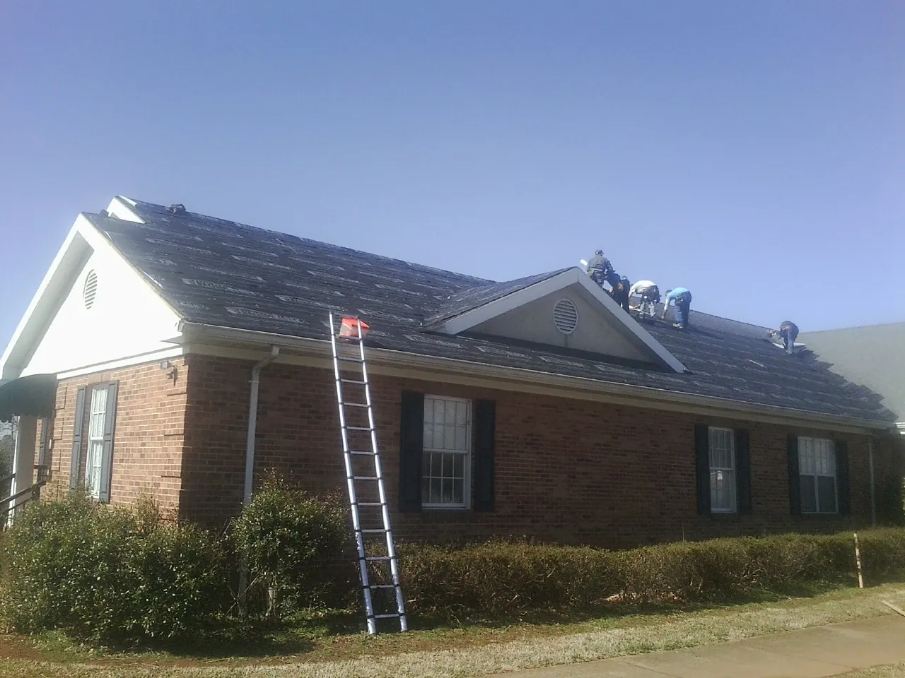 Crew tearing shingles off a brick ranch roof with a ladder set — Metal Roof Repair work by our crew in Hamlin