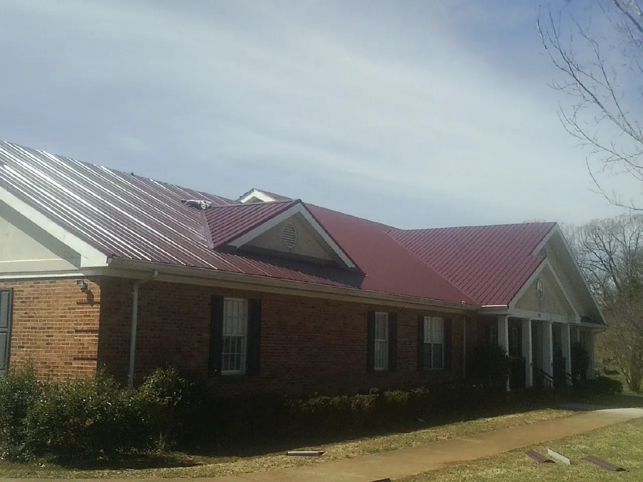 Red metal roof with gabled entries on a long brick building, from a Hail Damage Roof Repair job in Hamlin