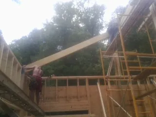 Carpenter raising a rafter beam on a new second story frame in Hamlin